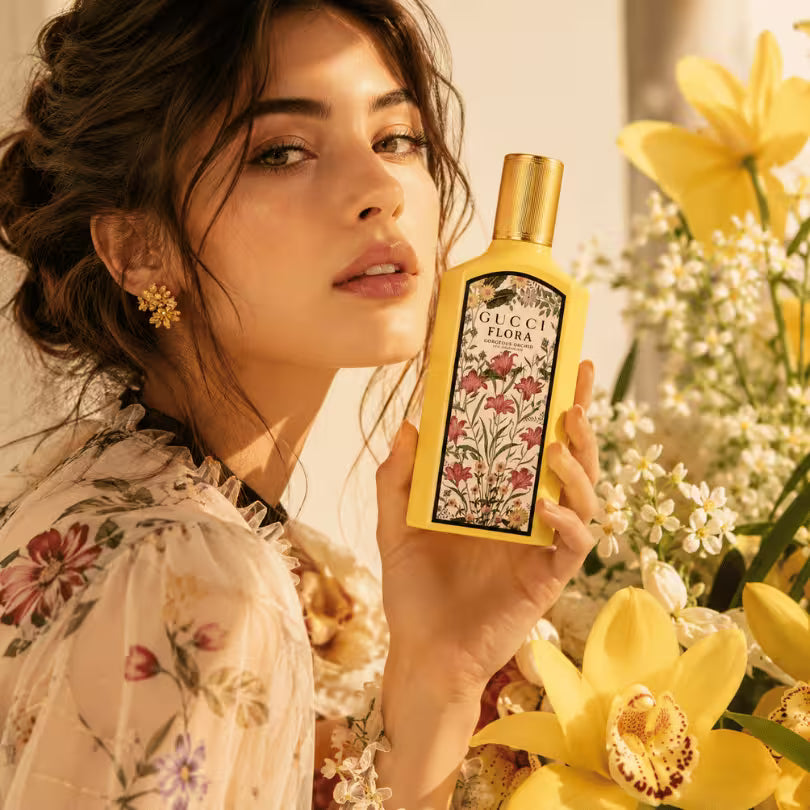 Female model holding Gucci Flora Gorgeous Orchid Eau de Parfum 150ml in a luxury floral setting